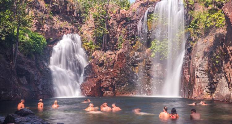 People swimming near a waterfall in a natural setting.
