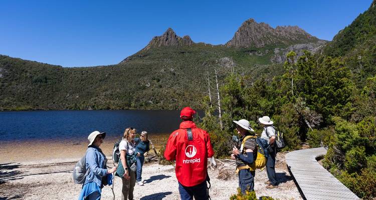 Group of hikers by a lake with mountain peaks in the background.