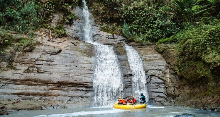 Gele rubberboot met gehelme avonturiers drijft aan de voet van een oerwoudwaterval in een smalle canyon.