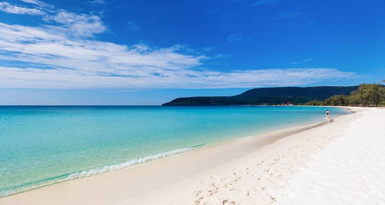 Plage de sable blanc immaculé avec une personne qui fait du jogging.