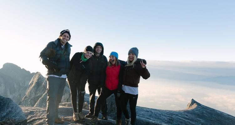 Five people posing on a mountain summit with clouds.