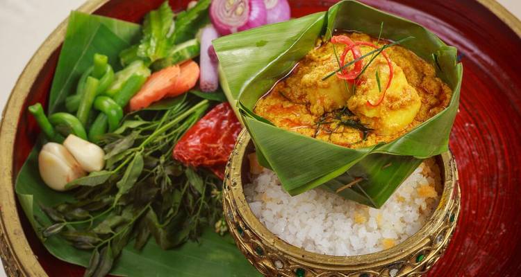 Nourriture asiatique traditionnelle servie dans un bol en feuille avec diverses herbes.