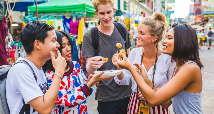 Groupe d'amis savourant de la nourriture de rue dans un marché animé.