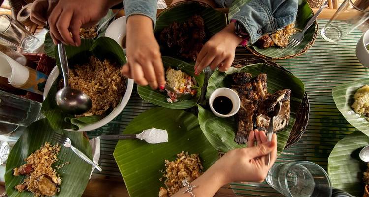 A table with hands serving traditional Filipino food on banana leaves.