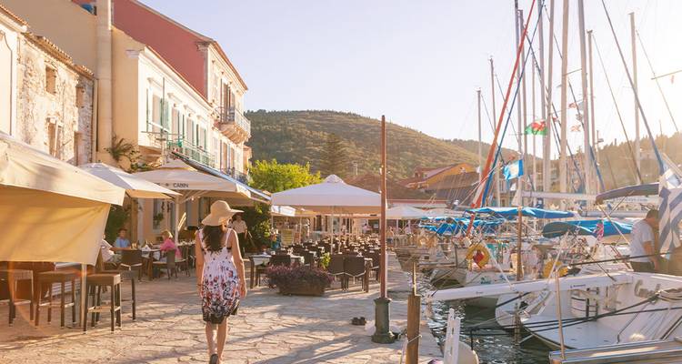 Person walking along a marina with cafes and moored boats.