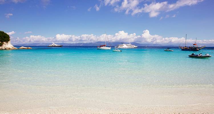 White sandy beach with clear blue water and boats.