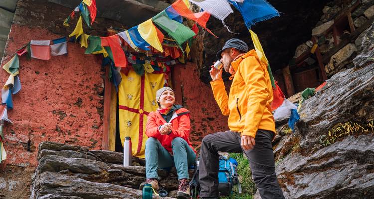 Excursionistas disfrutando de un descanso en un sitio budista decorado con banderas de oración.
