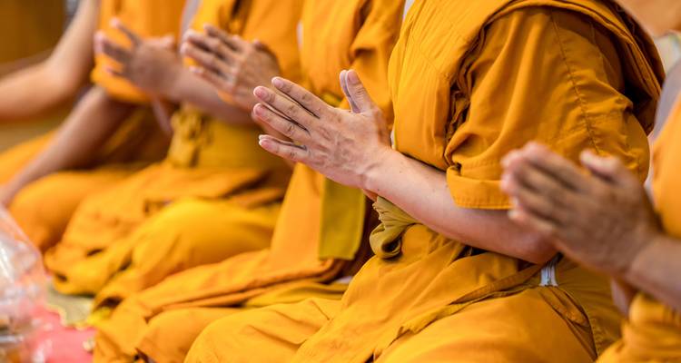 Grupo de monjes en túnicas naranjas sentados con las manos en posición de oración.