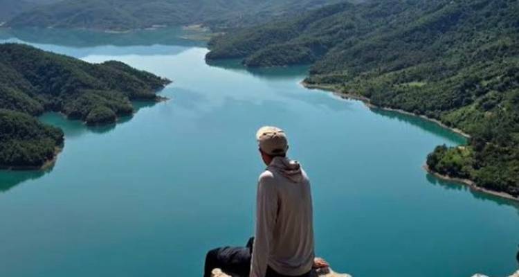 Personne assise au bord d'une falaise surplombant un lac.