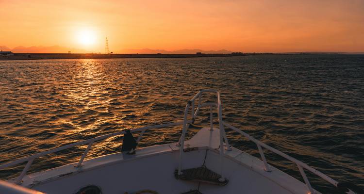 Vista de barco al atardecer sobre una masa de agua con montañas distantes.