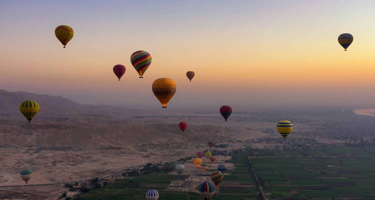 Globos aerostáticos volando sobre un paisaje agrícola y desértico al amanecer.