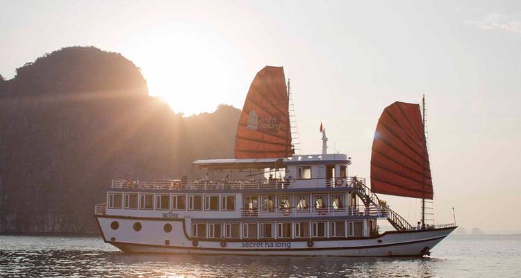 Barco tradicional navegando en la Bahía de Halong durante el atardecer.
