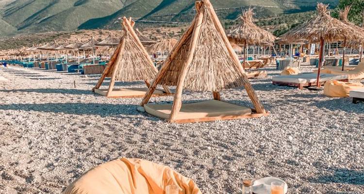 Installation de plage avec cabanes et transats sur un rivage de galets.