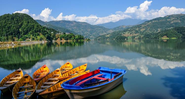 Bateaux colorés sur un lac serein avec des reflets de montagnes.