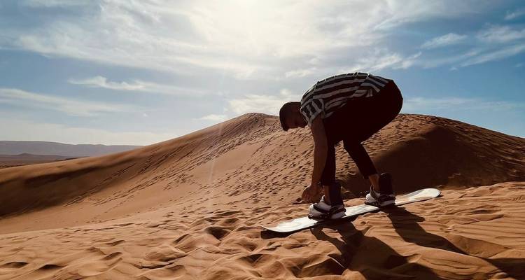 Une personne faisant du sandboard sur une dune de sable sous un ciel lumineux.