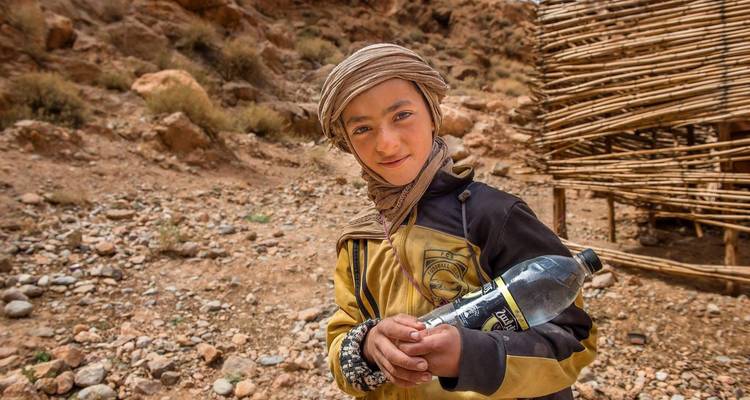 Un jeune enfant en tenue traditionnelle marocaine tenant une bouteille.
