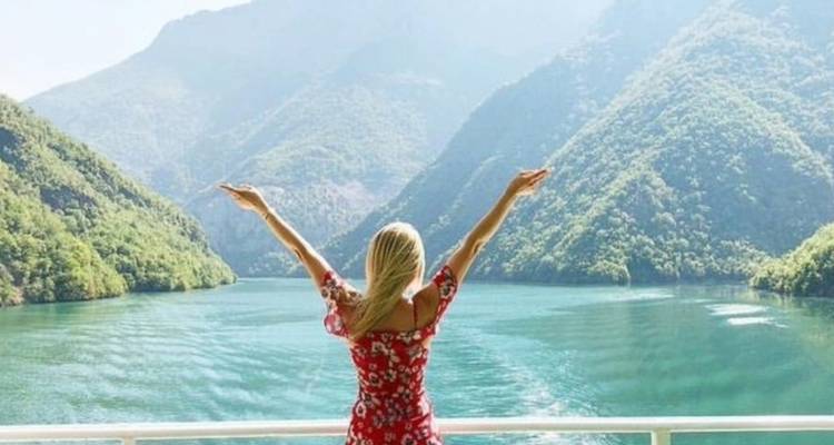 Personne debout les bras étendus devant une rivière pittoresque et des montagnes.