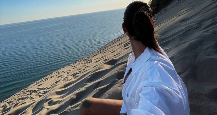 Une personne assise sur une dune de sable qui surplombe l'eau.