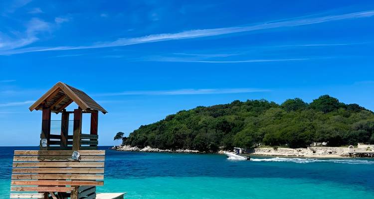Une plage avec une eau bleue claire et un poste de secours en bois.