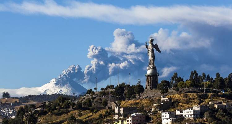 Panoramisch uitzicht op Quito met een monument en vulkanische as op de achtergrond.