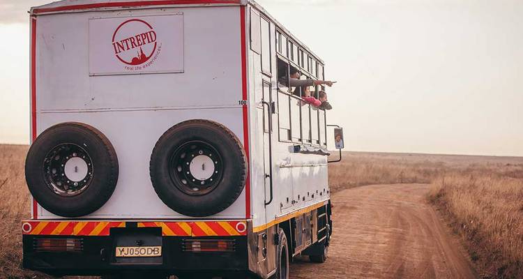 Safari truck op een onverharde weg in een open savanne landschap.