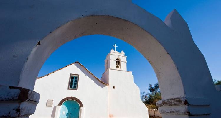 A white church with an arch entrance under a clear blue sky.