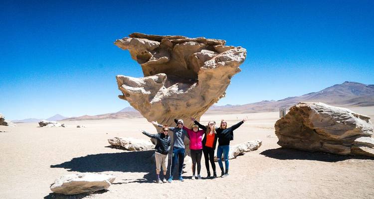 A group of people posing in front of a large rock formation in a desert.
