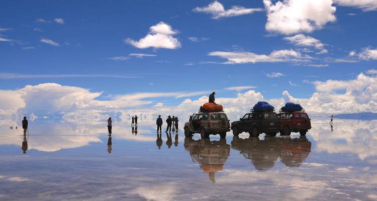 People and vehicles reflected on a mirrored salt flat.