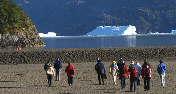 Group of people walking on the beach with glaciers in the background.