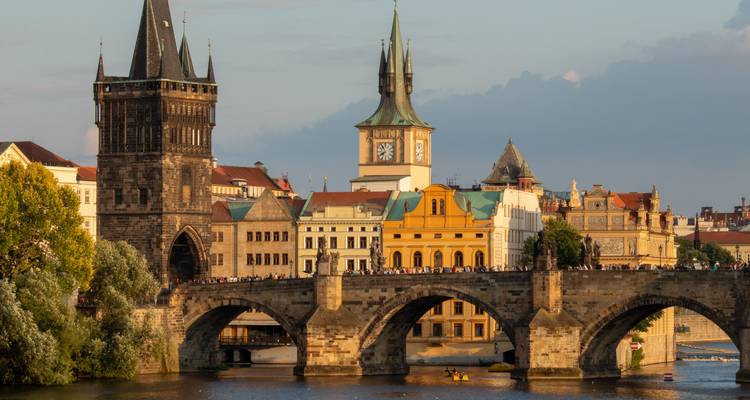 Historischer Uhrenturm und Brücke in Prag mit spazierenden Menschen.