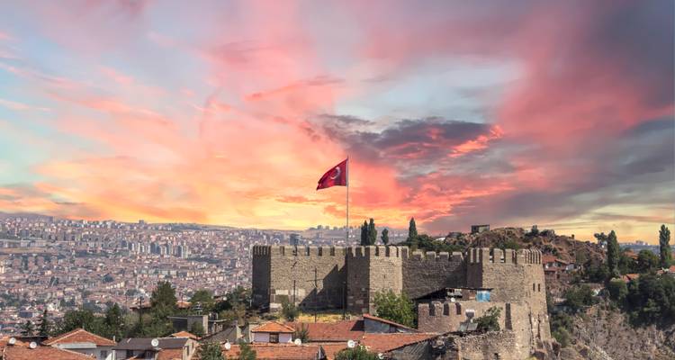 Castle with a Turkish flag at sunset overlooking a city.