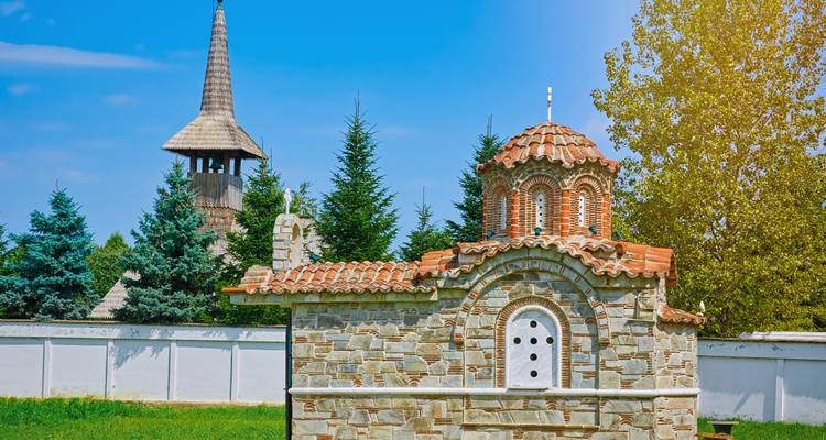 Pequeña iglesia con techo de tejas y árboles al fondo.