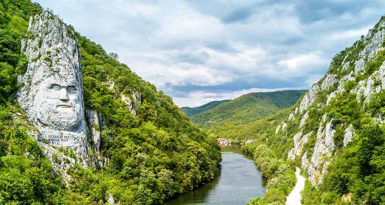 Rock sculpture of Decebalus along the Danube River surrounded by forested hills.
