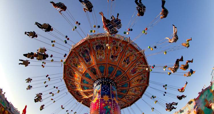 Manège à balançoires dans une fête foraine avec des gens qui profitent du manège sous un ciel bleu.