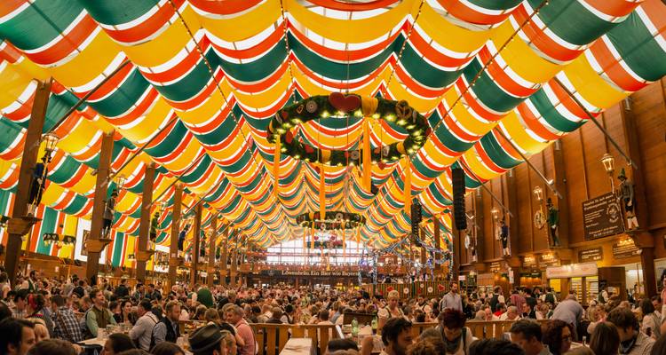 Tente de festival intérieure avec des personnes assises sous des bannières colorées et des lumières.