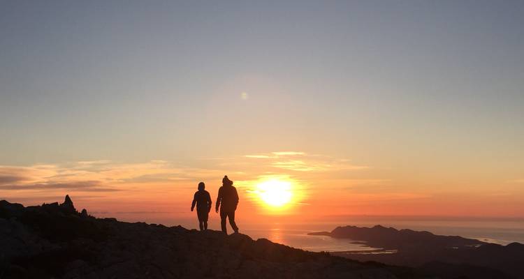Silhouetted hikers walking towards a setting sun over the mountains.