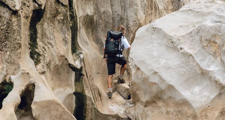 Un voyageur à sac à dos escalade à travers des formations rocheuses calcaires étroites en portant un grand sac à dos.