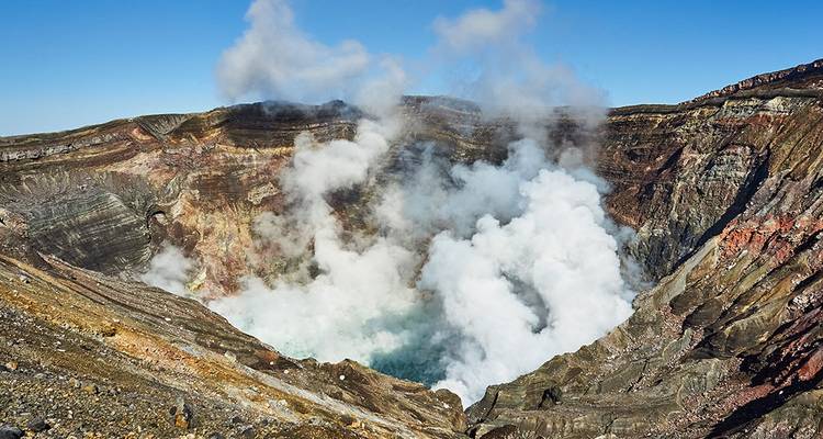 Cratère volcanique actif avec de la vapeur qui s'élève sous un ciel dégagé.