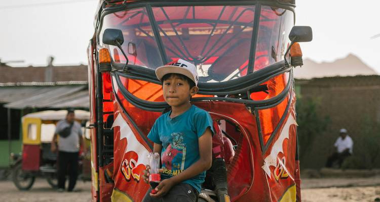 Een kind zittend op een geparkeerde driewieler op een stoffige straat.