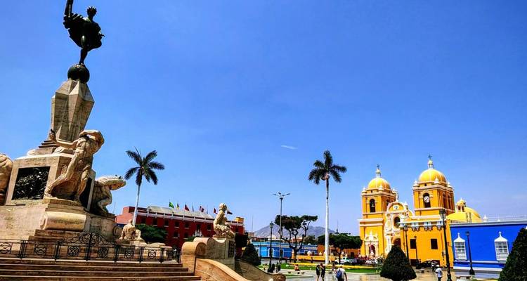 Plein met een standbeeld en gele kathedraal onder een blauwe hemel.