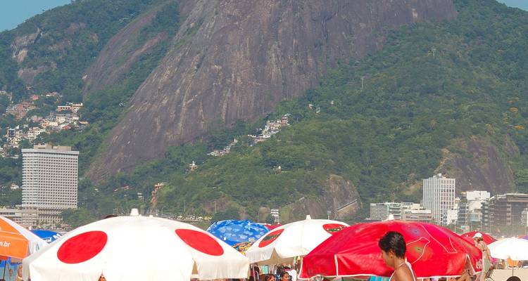 Plage bondée avec des parasols colorés et une montagne rocheuse.