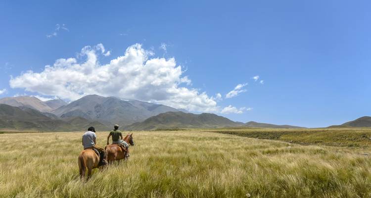 Deux personnes à cheval dans un vaste champ avec des montagnes au loin.