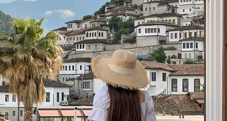Une femme portant un chapeau regardant les maisons de pierre blanche sur une colline.