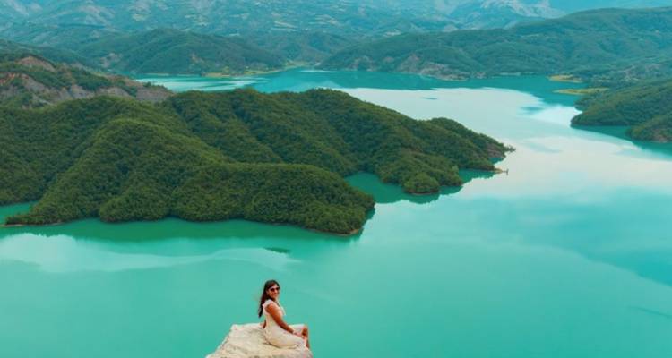 Femme assise sur une falaise surplombant un vaste lac avec des îles boisées.