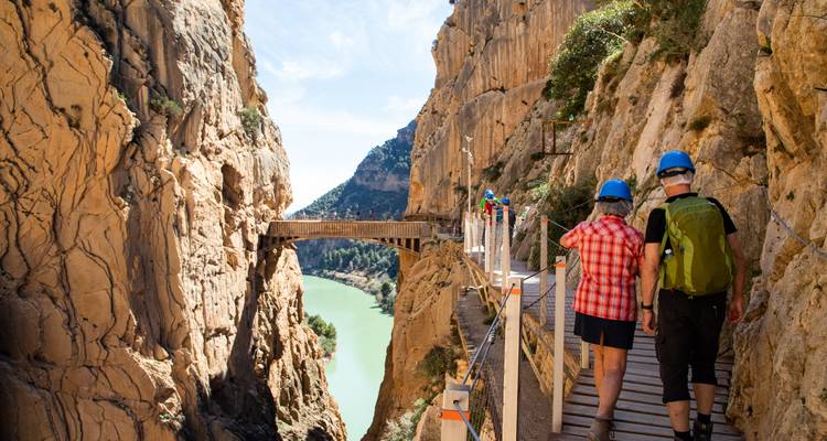 People walking on a narrow footpath along a cliff with a river below.