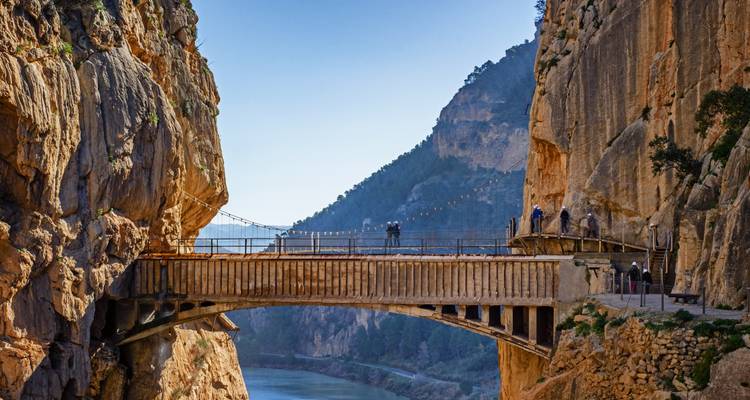 People crossing a bridge in a dramatic cliff setting.