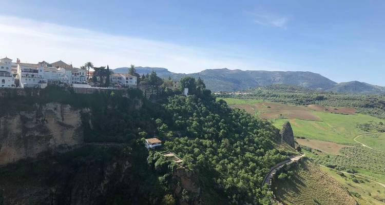 Dramático pueblo blanco en lo alto de un acantilado de Ronda con valle verde y montañas distantes bajo cielo azul