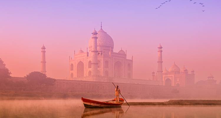The Taj Mahal reflected in water with a boat in the foreground at dawn.
