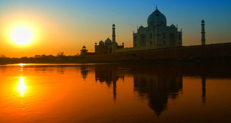 Silhouette of Taj Mahal at sunset with a vivid reflection on the river.