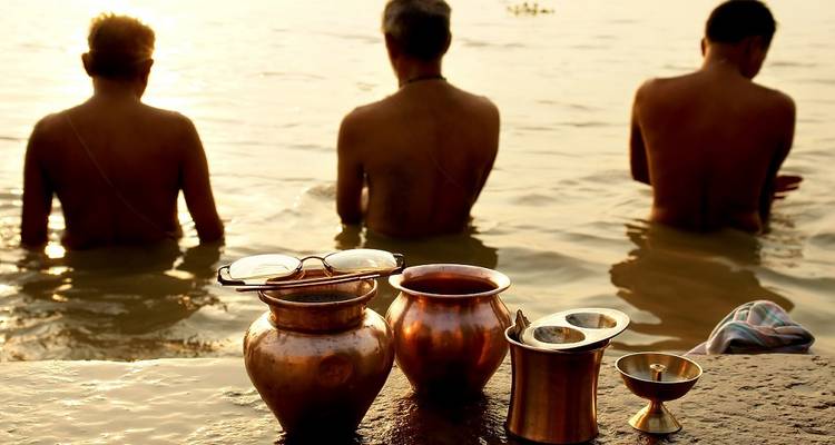 Three men performing a ritual in a river with golden pots.